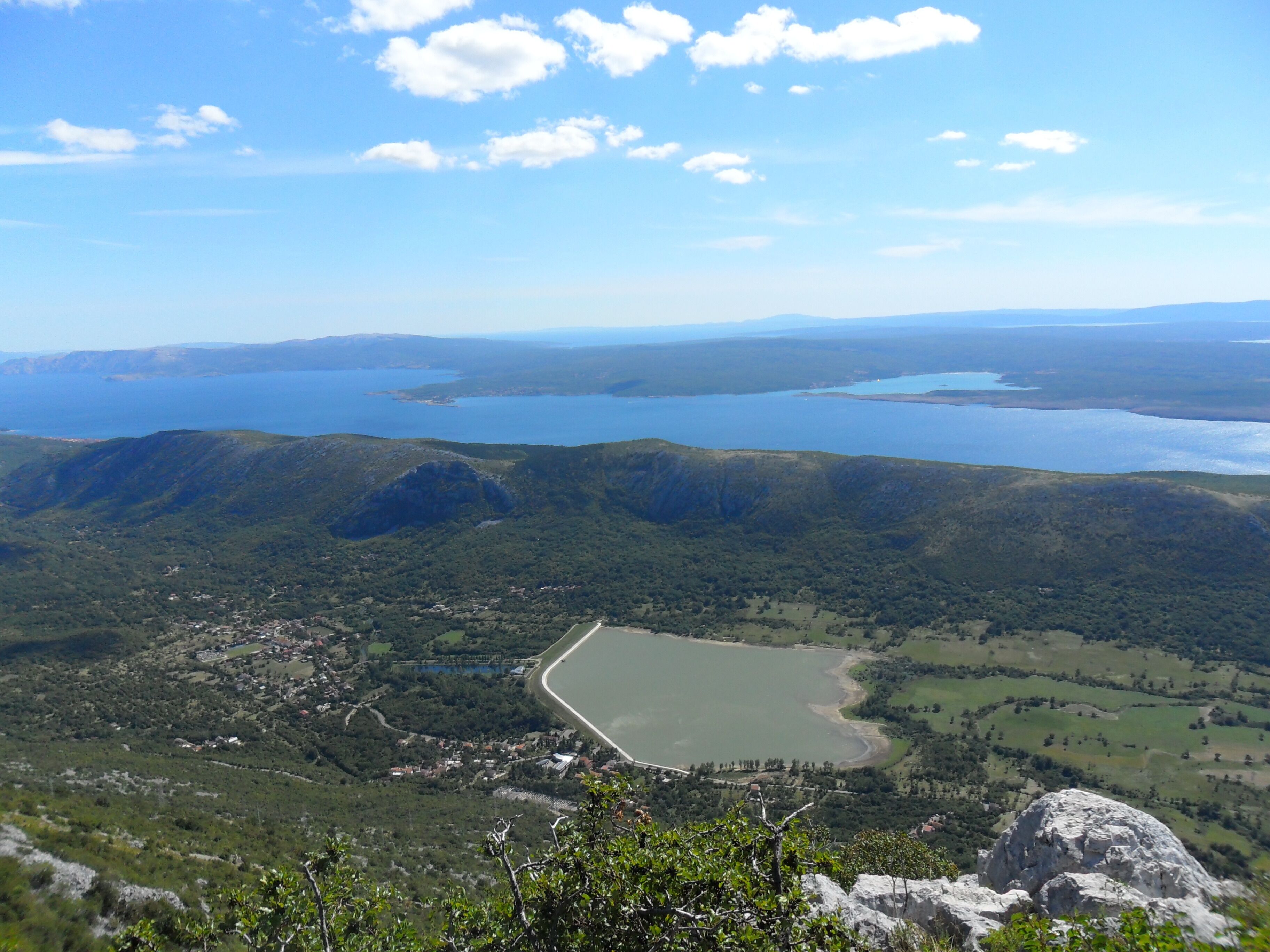 A panoramic view of a coastal landscape with multiple lakes, green hills, and a small settlement with visible buildings and roads.