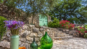 A stone wall with a green door, a stone staircase, and a vase with purple flowers.