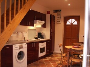 A compact kitchen with wooden cabinets, a built-in washing machine, and a dining area with a table and chairs.
