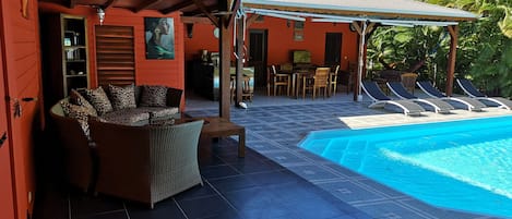 A covered outdoor area with a pool, lounge chairs, and a dining area.