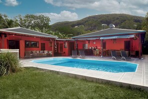 Un edificio rosso con piscina, area salotto esterna e vista su una collina.