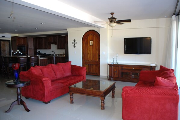 A spacious living room with a red sofa set, a coffee table, and a television mounted on the wall. - Luxury Home in Pedregal with Infinity Pool and Elevator. Walk to Town and Beach! (Cabo San Lucas)