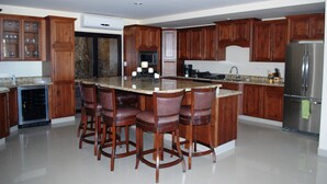 Une cuisine avec des armoires en bois, un comptoir en granit, un réfrigérateur en acier inoxydable et un îlot central intégré avec des tabourets de bar.