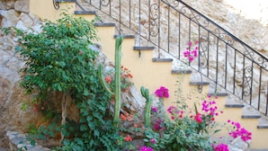 Un escalier en pierre orné d’une rampe en fer forgé, entouré d’une végétation luxuriante et de fleurs aux couleurs vives.