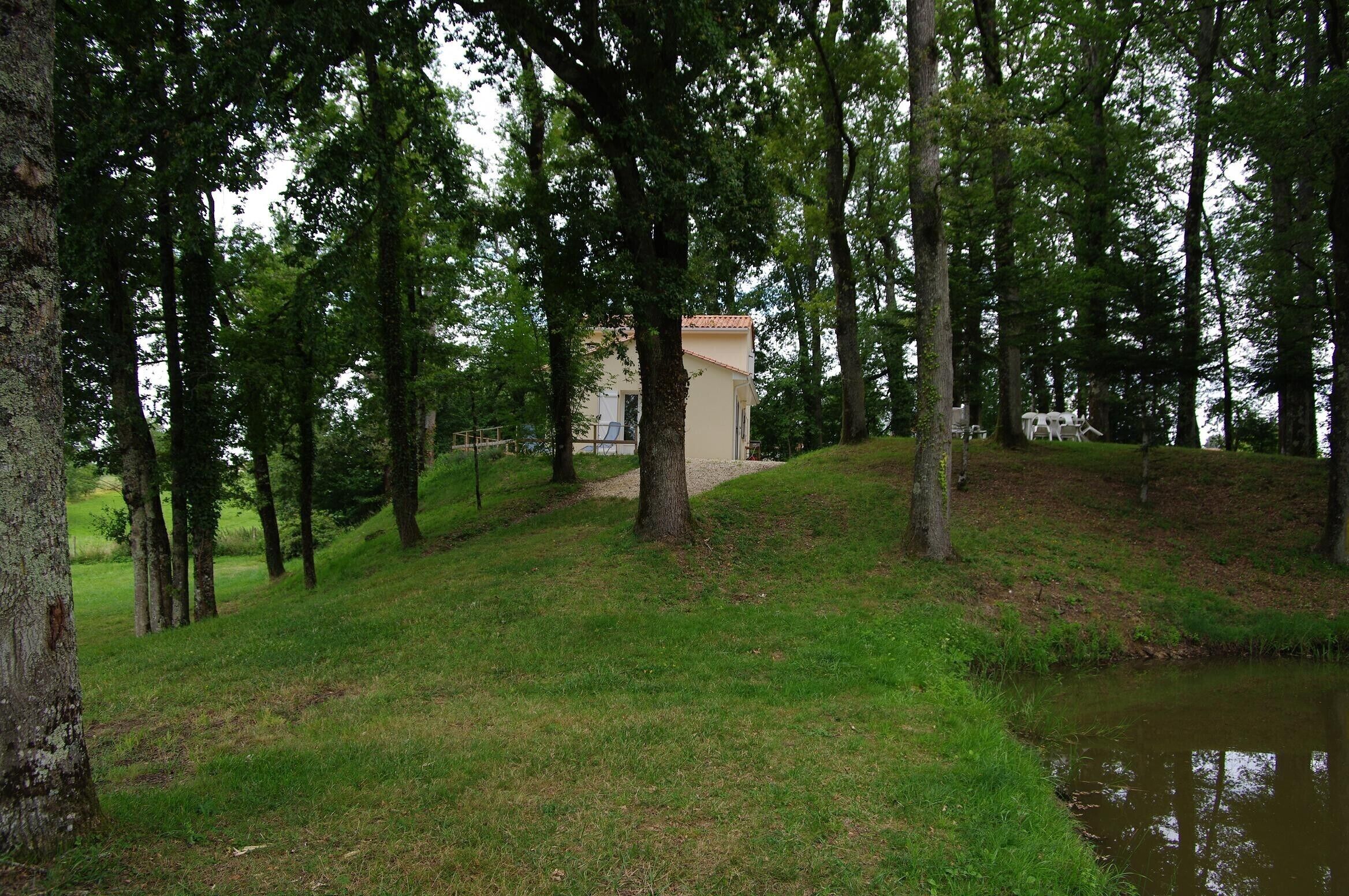 Un parque tranquilo con un edificio pequeño, rodeado de árboles altos y un estanque.