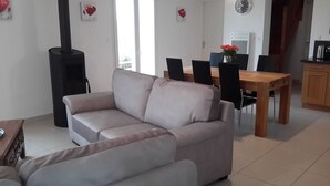 Ein Wohnzimmer mit einer Couch, einem Esstisch mit Stühlen, einer Kaffeemaschine und einer Uhr an der Wand.