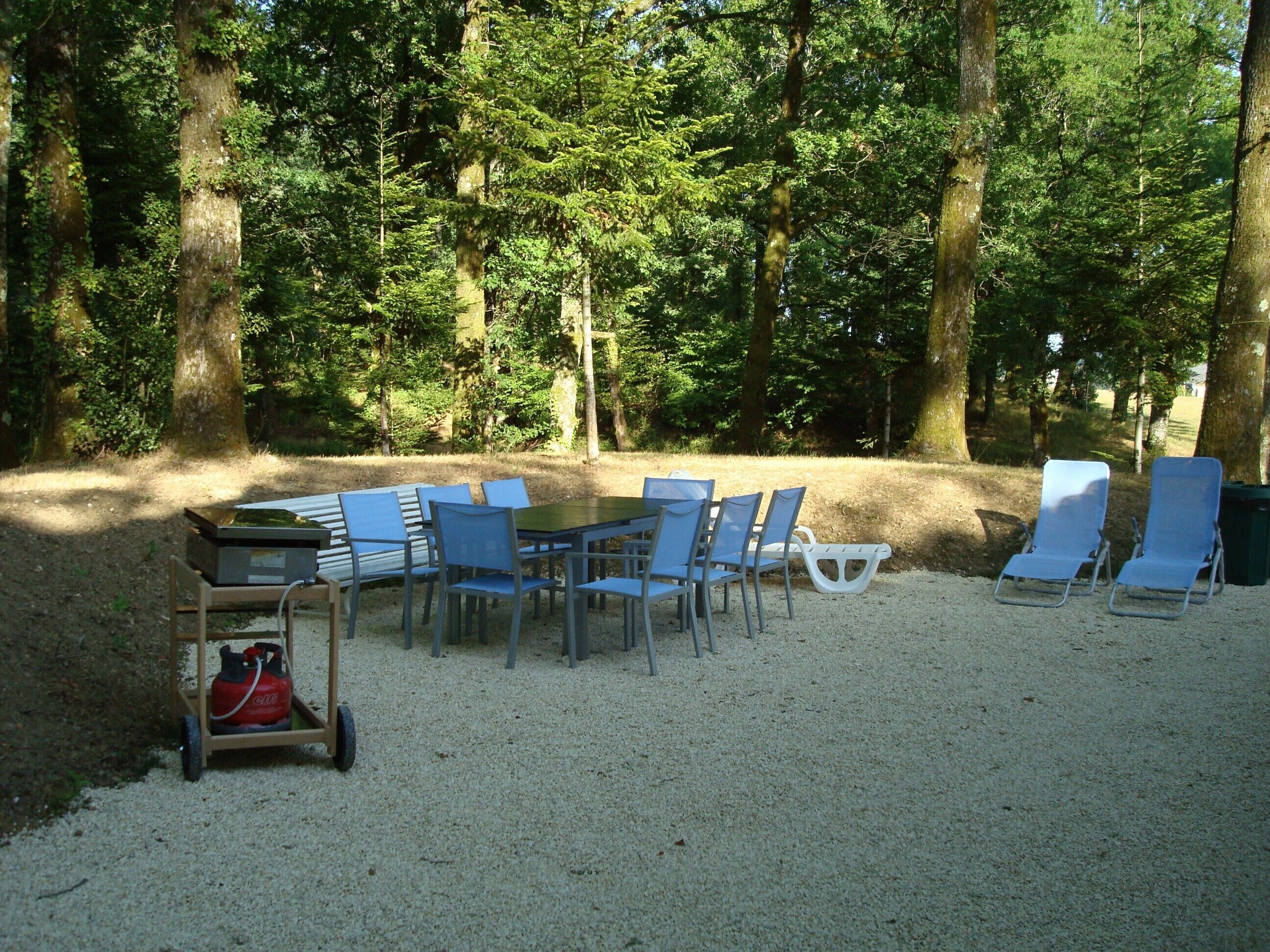 A table and chairs set up in a forested area with a gravel ground.
