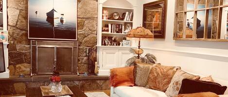 A living room with a stone wall, a flat-screen TV, a bookshelf, and a window with a view.