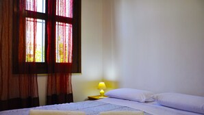 A hotel room with a bed, pillows, a nightstand with a lamp, and a window with curtains. - Cottage in the lemon grove on the sea (Lido di Noto)