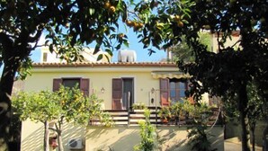 A house with a yellow facade, wooden shutters, and a small front garden with a tree and a bicycle. - Cottage in the lemon grove on the sea (Lido di Noto)
