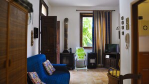 A living room with a blue sofa, a television, a fireplace, and a window with curtains. - Cottage in the lemon grove on the sea (Lido di Noto)