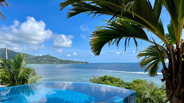An infinity pool with a wooden deck, surrounded by tropical foliage and overlooking a beach with clear blue water and distant hills. - Chalets Bougainville
Ground floor Apartment with Ocean View (Bougainville)