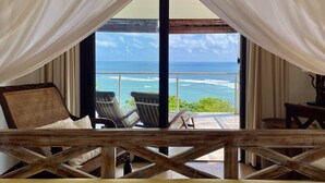 A room with a view of the ocean, featuring a bed, two chairs, and a small table. - Chalets Bougainville
Ground floor Apartment with Ocean View (Bougainville)