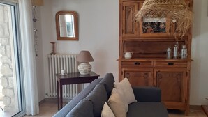 A living room with a grey sofa, a wooden cabinet, a mirror, and a hanging light fixture. - 200 meters from the heart of the village, App 55 M² WiFi In a closed courtyard, quiet (Châteauneuf-De-Gadagne)