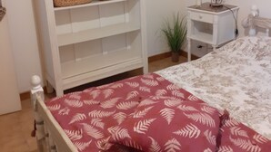 A bedroom with a bed, a white wardrobe, two wicker baskets, a bedside table with a lamp, and a small plant. - 200 meters from the heart of the village, App 55 M² WiFi In a closed courtyard, quiet (Châteauneuf-De-Gadagne)