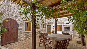 Un bâtiment en pierre avec une porte en bois, une table entourée de chaises et une vigne grimpante.