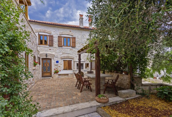 A stone building with a courtyard, wooden shutters, and a table with chairs.