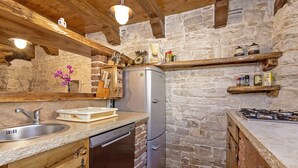 Une cuisine avec un mur en pierre, des poutres apparentes, un réfrigérateur en acier inoxydable et un lave-vaisselle encastré.