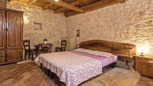 Una habitación rústica con cama de madera, paredes de piedra y un armario de madera.
