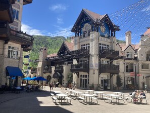 A building with a clock tower, outdoor seating, and string lights.
