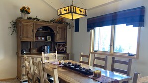 Un comedor con una mesa y sillas de madera, una araña y una ventana con vistas a árboles.