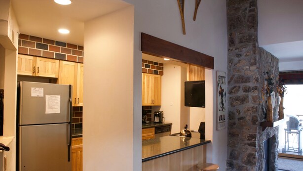 Cocina con alacenas de madera, pared de acento de piedra, refrigerador y una barra con taburetes.