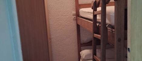 A small, compact room with a bunk bed, a wooden wardrobe, and a light fixture on the wall.