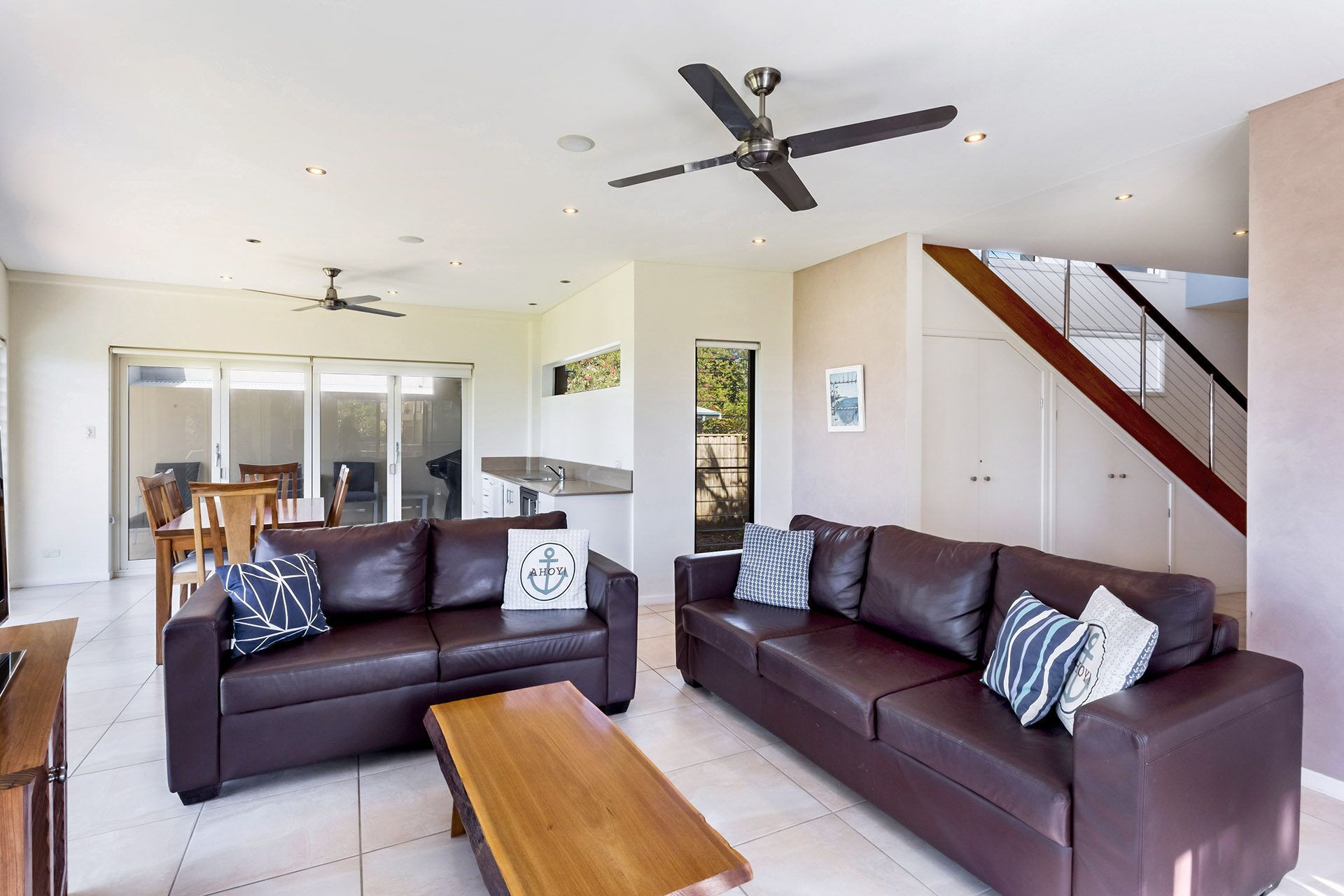 A modern living room with two dark brown leather sofas, a wooden coffee table, and a ceiling fan.