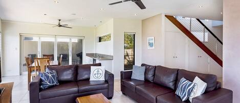 A modern living room with two dark brown leather sofas, a wooden coffee table, and a ceiling fan.
