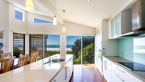 Una cocina moderna con una isla grande, armarios blancos y vista al océano.