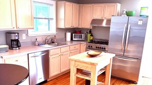 A compact kitchen with wooden cabinets, a stainless steel refrigerator, a microwave, a stove, and a dining table with chairs. - Downtown Kennebunk Home  (Kennebunk)