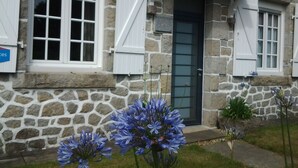 A stone house with a dark door and white shutters, featuring a small garden with blue flowers. - House 2-7 people, 150m from the beach Tregastel White Strike, Near Perros-Guirec (Trégastel)