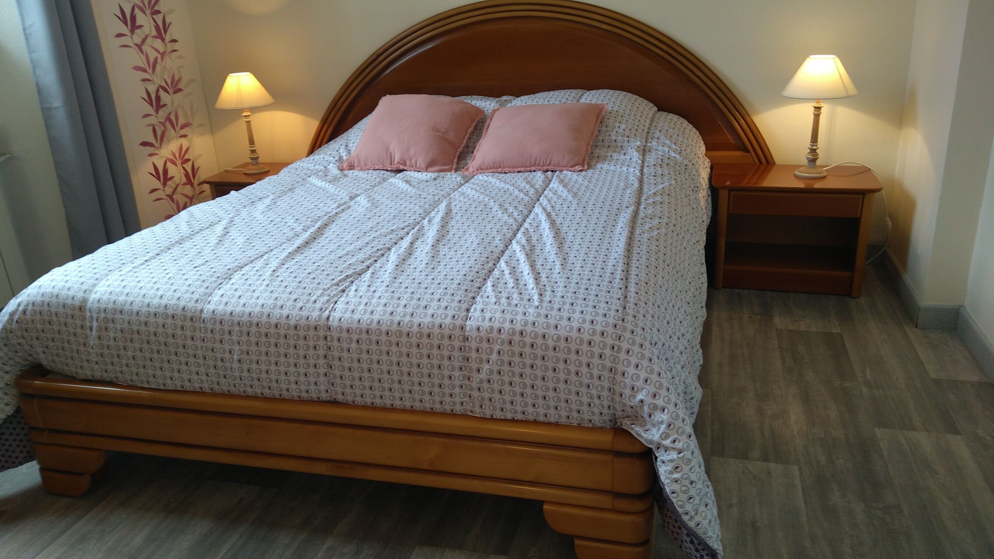 Un lit bien fait, avec une tête de lit en bois, deux lampes de chevet et une couvre-lit à motifs.