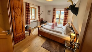 Un dormitorio acogedor con cama de madera, un radiador, una ventana con cortinas y una decoración de cabeza de ciervo montada en la pared.