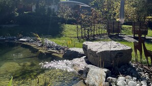 Un entorno tranquilo al aire libre con un estanque despejado, rocas y una terraza de madera.
