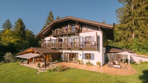 Un chalet de dos pisos con balcón, un porche cubierto y un césped bien cuidado.