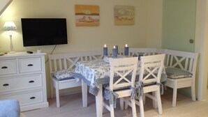 A cozy room with a white bench, a table with checkered tablecloths, and candles. There are paintings on the wall and a television on a stand. - quiet duplex apartment, modern and bright (Sylt-Ost)