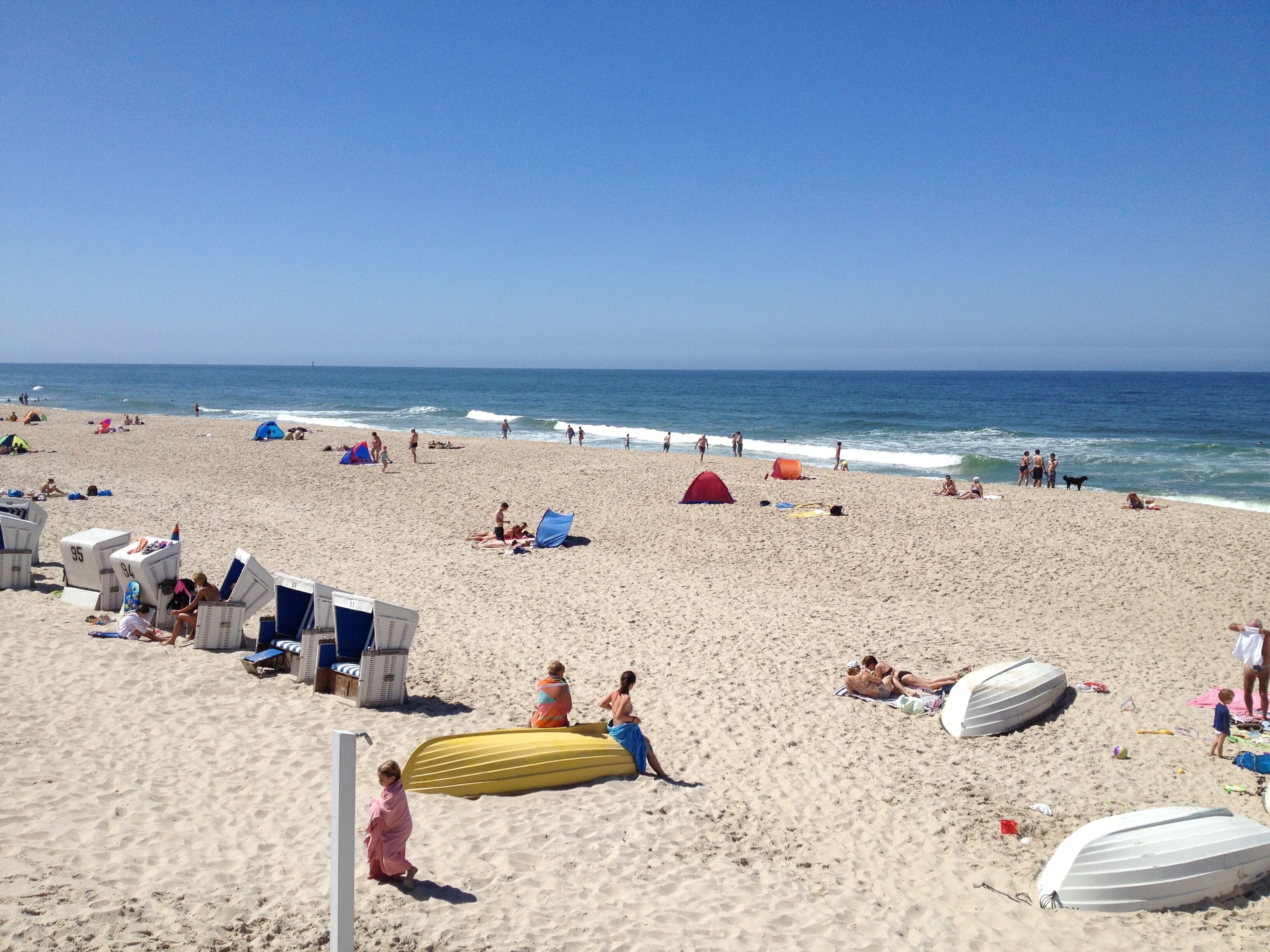A beach with sun loungers, umbrellas, and a few tents.
