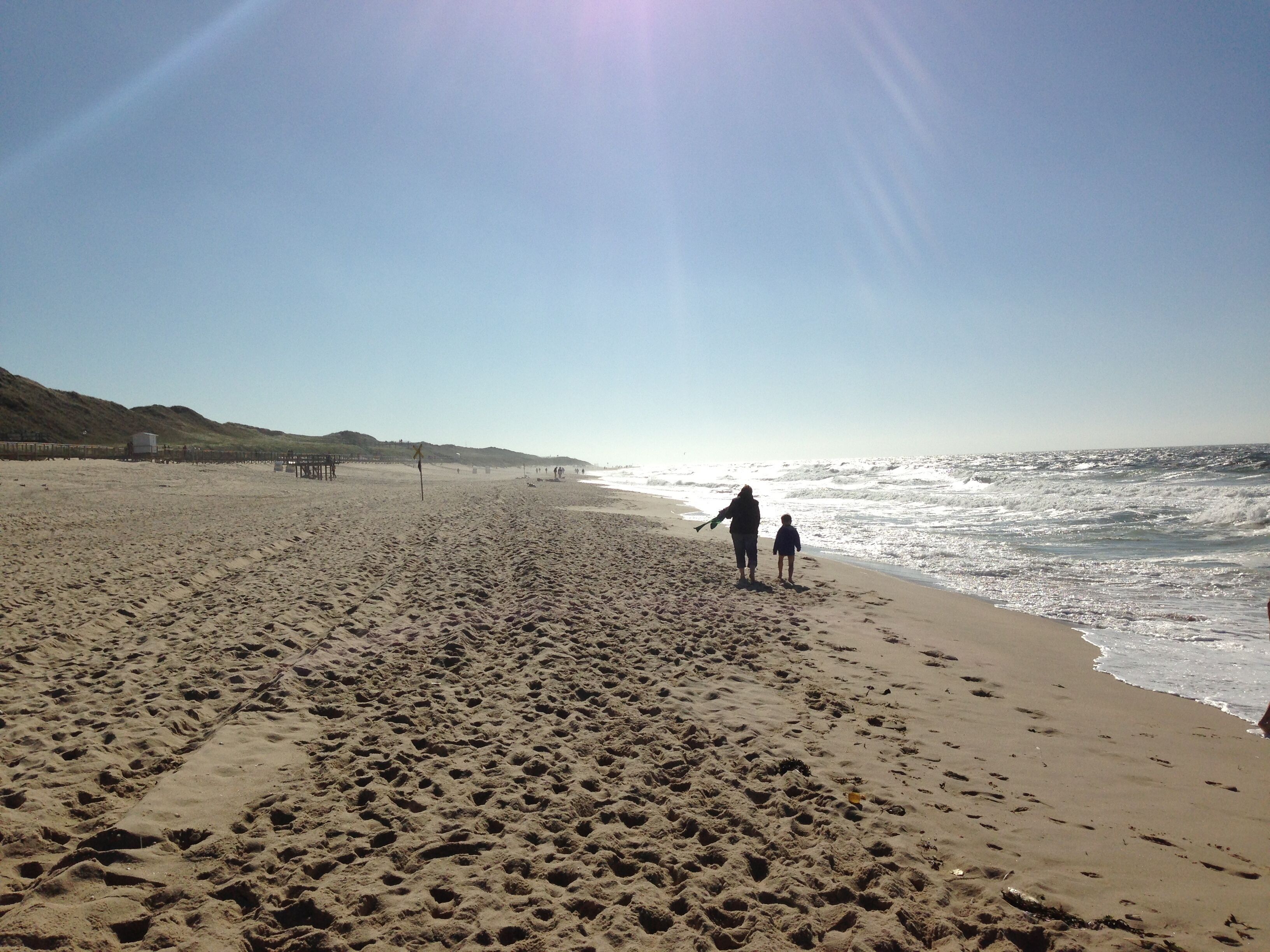 A wide sandy beach with footprints, a clear sky, and a calm sea.
