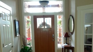 Un pasillo con una puerta de madera, una planta en maceta, un espejo y una lámpara.