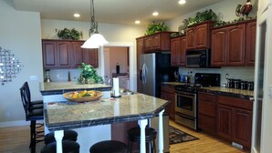Una cocina moderna con armarios de madera, encimeras de granito, una isla central con taburetes y electrodomésticos de acero inoxidable.