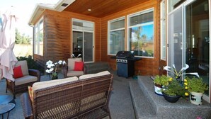 Un patio cubierto con mobiliario de mimbre, una parrilla y plantas en macetas.