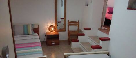 A bedroom with two beds, a wooden chair, a nightstand with a lamp, a mirror, and a window.