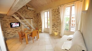 A cozy room with a stone wall, a wooden staircase, a white sofa, and a dining table with chairs. - Bastide du Soleil - Duplex studio 800 metres from the beach (CANNES)