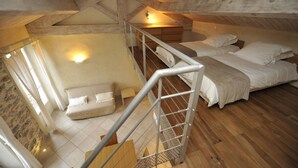 A loft bedroom with a wooden ceiling, a bed, a small seating area, and a staircase. - Bastide du Soleil - Duplex studio 800 metres from the beach (CANNES)