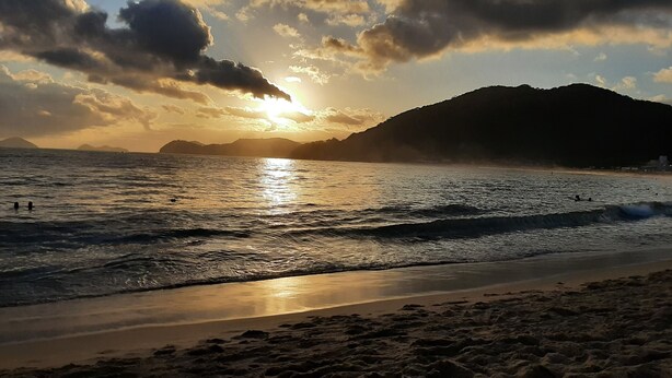 A beach with waves, a sunset, and mountains in the background. - House for rent in gated community, Boiçucanga, São Sebastião, SP (São Sebastião)