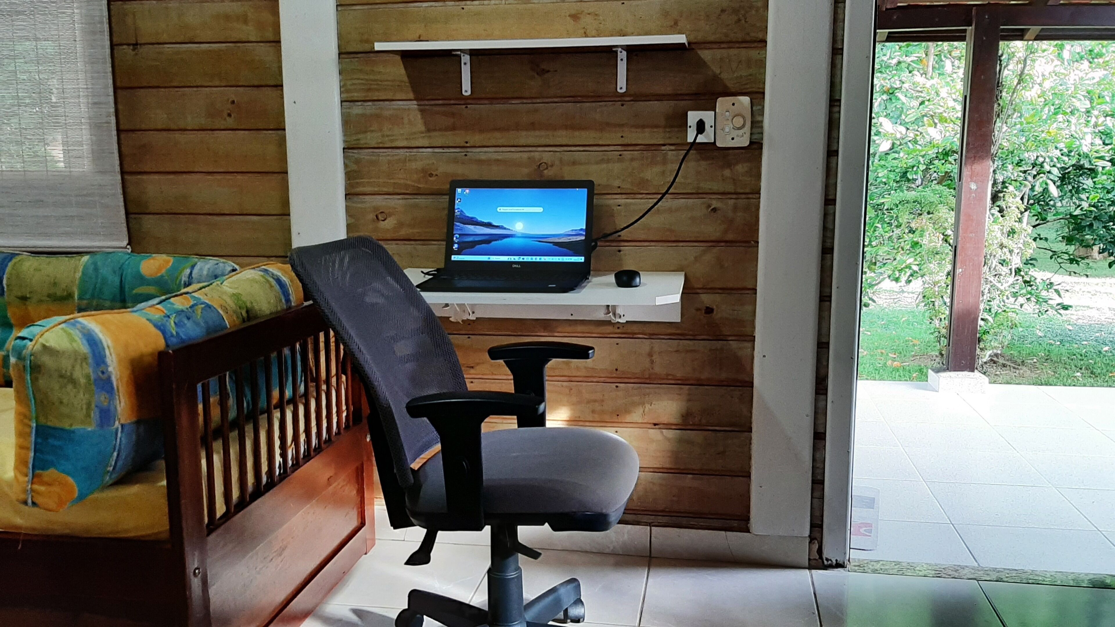 A room with a wooden wall, a desk with a laptop, a chair, and a sofa.
