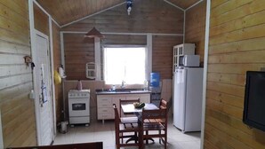 A compact kitchen with a dining area, wooden walls, a ceiling fan, and a TV mounted on the wall. - House for rent in gated community, Boiçucanga, São Sebastião, SP (São Sebastião)