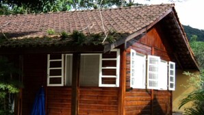 A wooden cabin with a tiled roof, a porch, and a small covered area. - House for rent in gated community, Boiçucanga, São Sebastião, SP (São Sebastião)