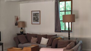 Una sala de estar con sofá, una mesita de madera, una lámpara, un radiador y una ventana con cortinas.